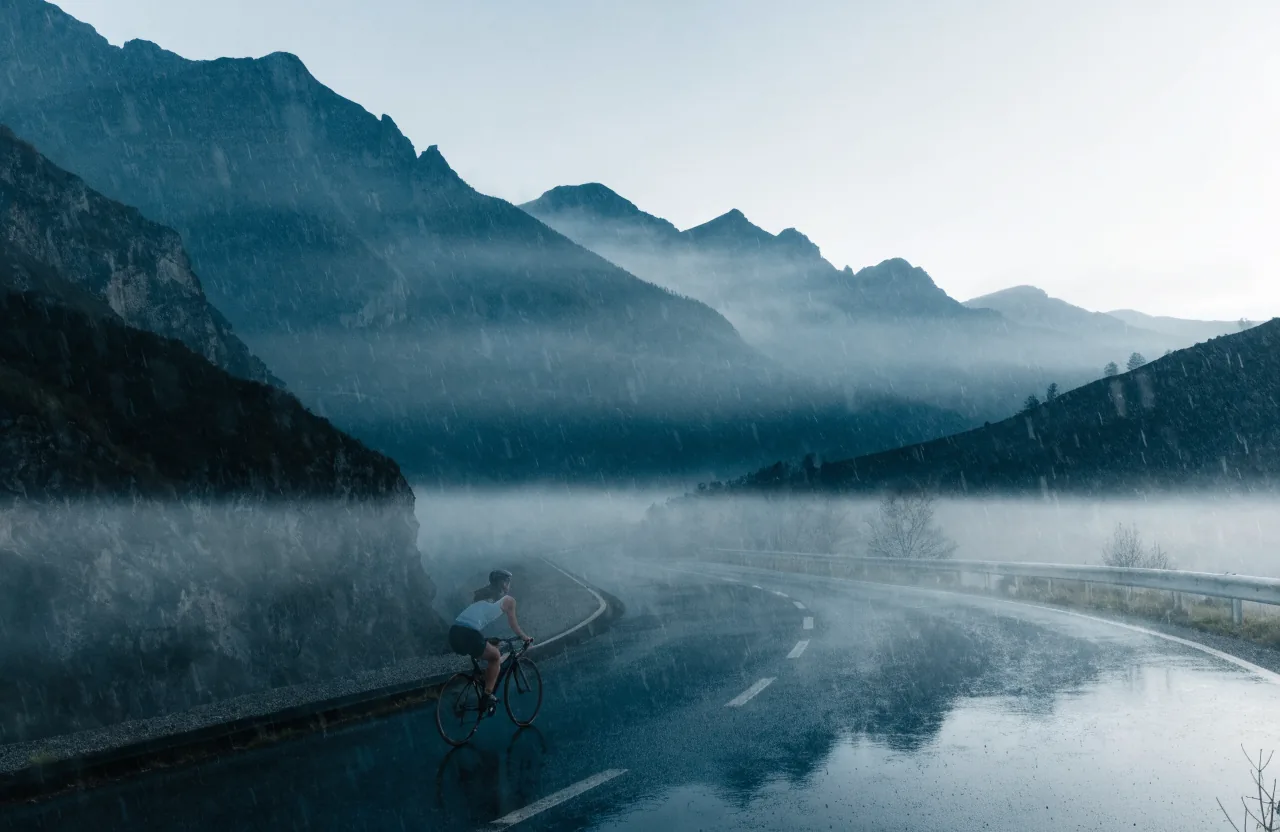Rennradfahrerin von hinten auf einer leeren Schweizer Passstrasse in der Morgendämmerung.