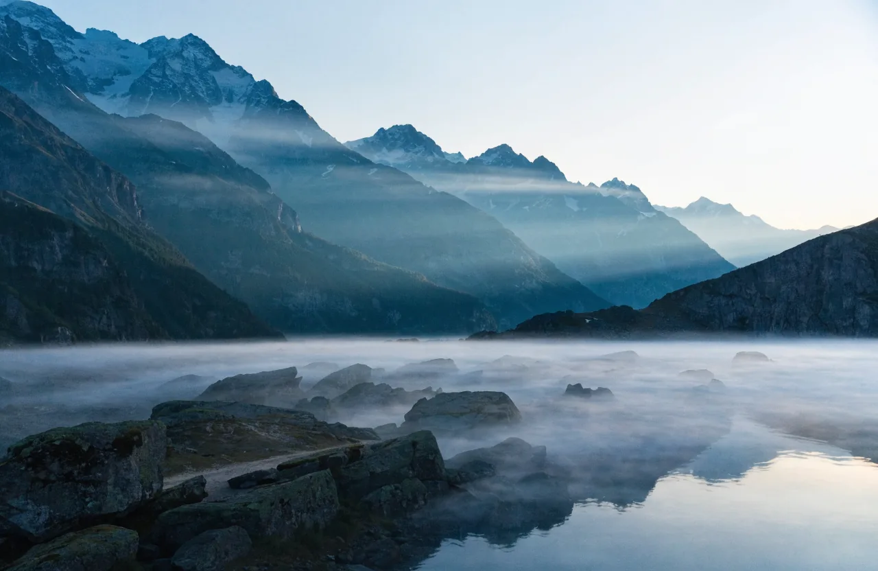 Menschenleeres Schweizer Alpenpanorama zur blauen Stunde, gestaffelte Bergketten in Nebelschichten.